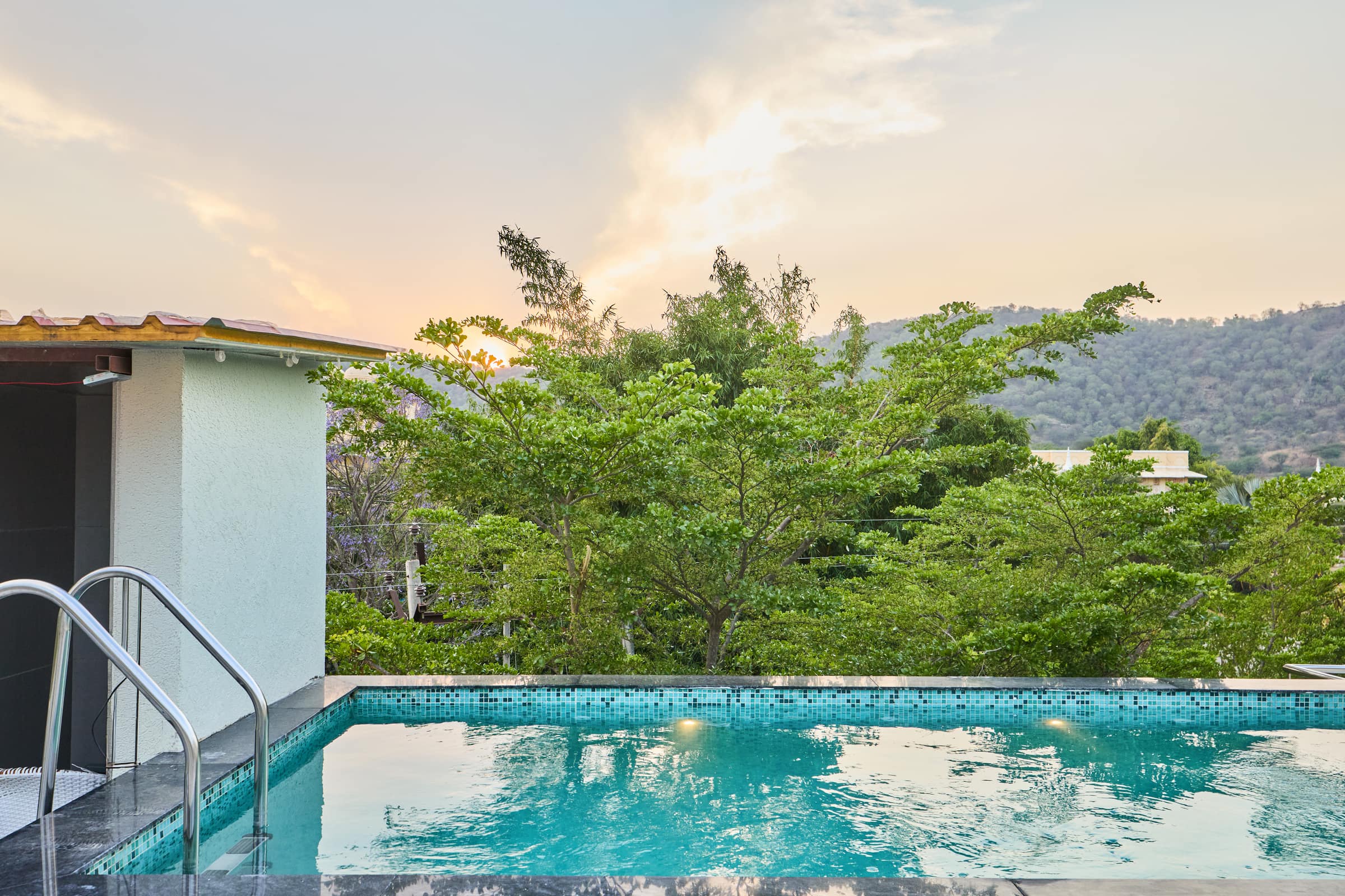 The rooftop plunge pool glowing at sunset with the Aravalli hills behind